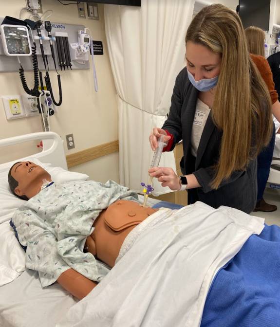 Student practicing bolus feedings through the PEG tube feeding using a 60-cc syringe on a manikin